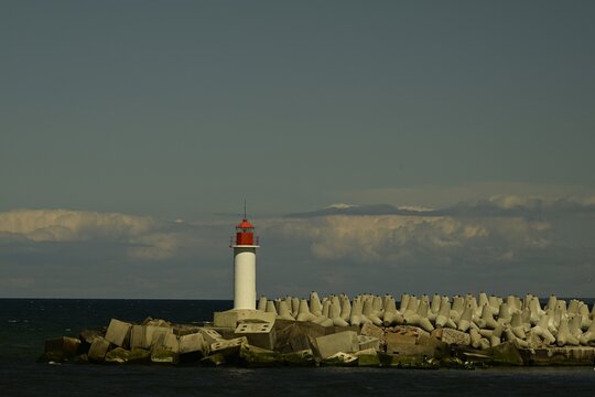 Red lighthouse on a breakwater with concrete tetrapods under dramatic cloudy sky