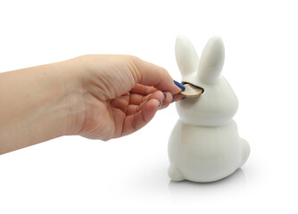 Hand putting 1 euro coin into money box in bunny or rabbit shape, isolated on white backgroung. Cash back, reserve and money saving concept.