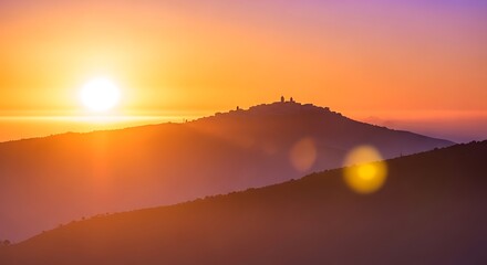 Sunset over a silhouette of a town on a hill with lens flare orange purple