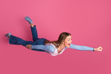 Charming young woman playfully mimics flying superhero pose against vibrant pink background...