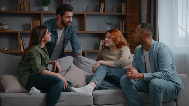 Four happy friends talking at home party stacking hands together unity friendship community group multiracial diverse women men on couch planning discuss agree stack arms teamwork cooperation support