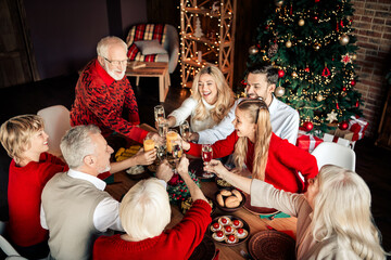 Family and friends celebrate Christmas together around a festively lit table with a Christmas tree and warm decorations