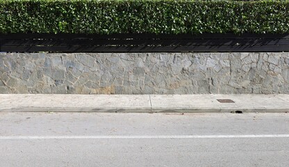 Fence made of green-gray stone wall with wood panels and hedge on top. Sidewalk and street in front. Urban background for copy space.
