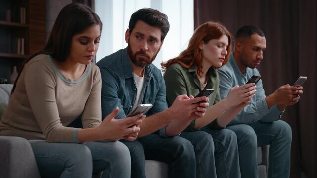 Four multiracial friends phones addicted frustrated man looking on buddies upset with ignore multiethnic men women at home party interested in mobile scrolling lost in gadgets overuse social media app