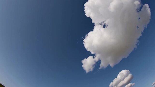 A single fluffy cloud against a clear blue sky, captured from a low-angle perspective, resembling a serene nature video scene. Live desktop wallpaper.