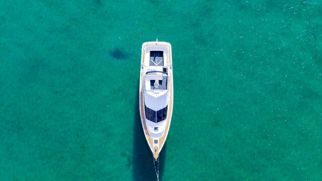 Aerial view of a lone white yacht cutting through the vibrant turquoise water, showcasing a stark contrast, Location data omitted.