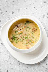 A bowl of creamy soup garnished with herbs and other ingredients, served on a white plate on a textured gray background.
