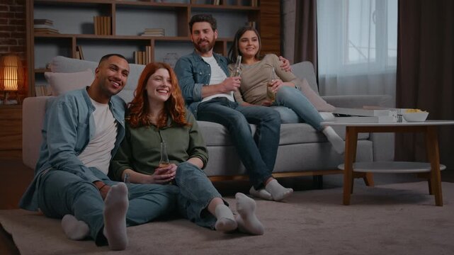 Carefree multiethnic four friends having fun watching tv at home party double date two couples watch television talking men laughing smiling women enjoying cinema movie film program friendship holiday