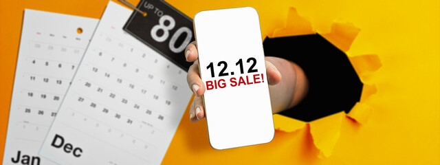 Human hand through hole paper showing 12.12 big sale text on cellphone screen with up to 80% text...