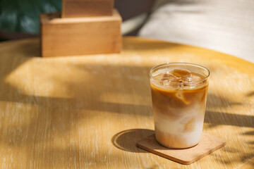 a glass of iced milk coffee on wooden table in sun light and shade