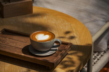 latte coffee art on wooden plate at desk in sun shine with shade of the tree