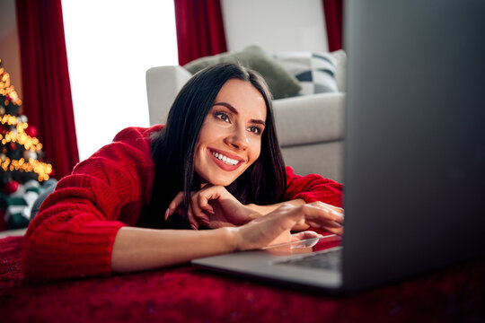 Smiling young woman wearing a red sweater using a laptop at home during the Christmas season with festive decor - Powered by Adobe