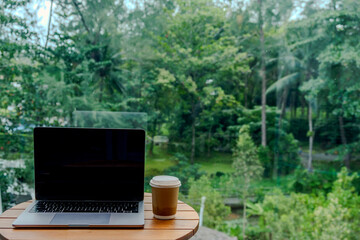 hot coffee cup on the round wooden table beside the laptop with blurred floor background