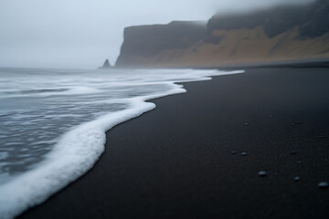 Fototapeta premium A serene seascape featuring a black sand beach with gentle waves lapping the shore, set against a backdrop of misty cliffs, evoking a sense of tranquility and natural beauty.