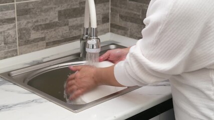 Women's hands washing a white plate in the sink