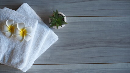 Top view of white towels with frangipani flowers and aloe vera plant on wooden background, creating a natural and peaceful spa atmosphere ideal for wellness, beauty, and relaxation concepts.