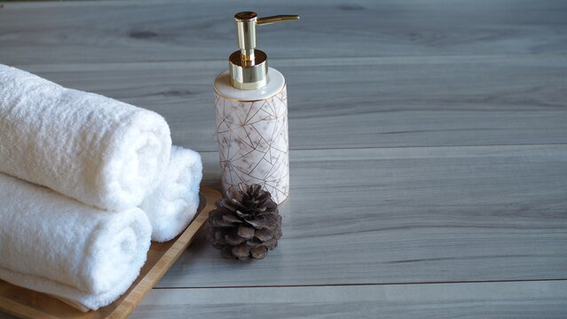 Luxury spa scene with white towels, marble soap bottles and pine flowers on wooden floor. Perfect for spa, beauty, hotel or skincare product advertising.