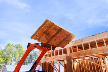 Forklift raises wooden osb board to complete framing of house under suburban neighborhood.