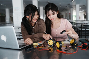 Asian female students and their teenage friends in high school chat and work together on homework to build a robot in the school cafeteria.