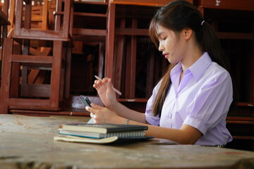 Asian female student in high school uniform doing homework and thinking about a school report.
