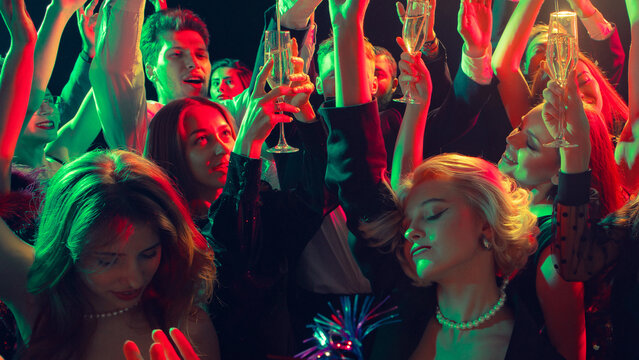 New Year toast with champagne glasses and happy faces glowing in colorful lights. Concept of festive nightlife, emotional unity, and luxury drink branding