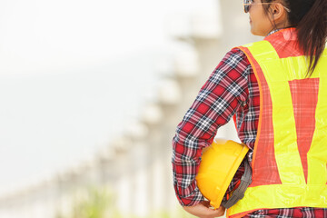 A construction worker observes a building site while holding a yellow hard hat, symbolizing safety...