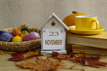 Calendar for November 23rd: a decorative calendar with the date 23, the month's name in English, colorful yarn, and a cup of tea with autumn leaves