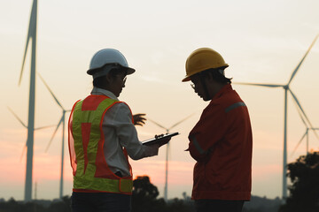 Engineers discuss wind turbine project at dusk, emphasizing teamwork and innovation in renewable energy.