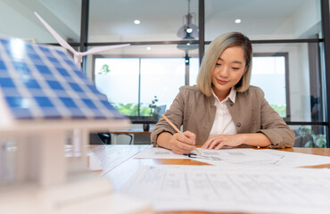 female architect working on blueprint for house real estate project, asian woman engineer sitting in office planning on project alternative clean environment energy for sustainable business	