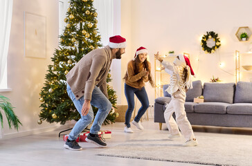 Family dancing with daughter at home on christmas. Parents in Santa hats play a lively game by the tree, laughing in a cozy living room. Captures family holiday joy and togetherness now.