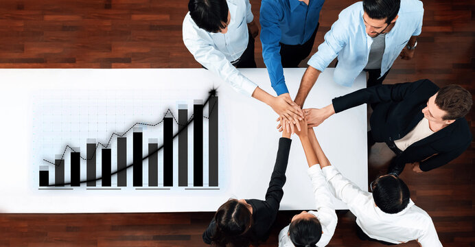 A diverse group of professionals engages in teamwork while placing their hands together in support of business growth, showcasing a bar graph on a conference table. Axiom