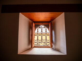Traditional Moroccan Architecture: Sunlit Ornate Wrought Iron Window Grille and Wooden Frame in a Historic Marrakech Interior