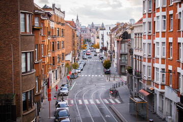 Obraz premium Urban European street with tram tracks, brick buildings and parked cars in Brussels. Perfect for concepts of city life, infrastructure, transportation and travel destinations.
