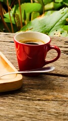 Warm red coffee cup on rustic wooden table with greenery background