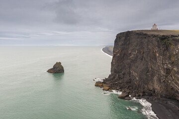 Steep cliff on the coast with a lighthouse under a grey sky, Dyrhólafjara, Dyrhólaey or Dyrholaey, south coast, Iceland