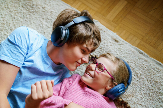 Two children, a teenage boy and a little girl, listening to music together with headphones. Smiling happy siblings enjoying sound and spending fun leisure time indoors.