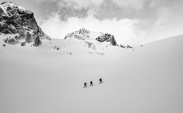 Three ski tourers in a lonely landscape, snow-covered mountain landscape, black and white photo, cloudy mood, high tour, Bernese Alps, Bernese Oberland, Switzerland - Powered by Adobe
