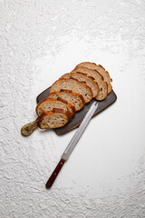 Sliced whole wheat sourdough bread with vintage knife on textured white background