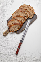 Sliced whole wheat sourdough bread with vintage knife on textured white background