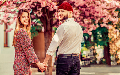 Naklejka premium Lovers couple holding hands in a sakura. Young loving couple holding hands. Young couple in love. The man holds the woman's hand