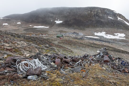 Cabin near scrap yard in rocky, hilly landscape with snow remains, arctic settlement Ittoqqortoormiit, Scoresbysund or Scoresby Sund or Greenlandic Kangertittivaq, East Greenland, Greenland