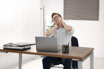 Naklejka premium Young businessman stretching his neck at table in office