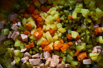 Top-down view of boiled potatoes, carrots, green peas, pickles, and sausage mixed in a bowl. Perfect festive preparation for Christmas or New Year Olivier salad.