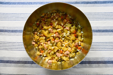 Top-down view of mixed vegetables, pickles, sausage, and boiled eggs in a metal bowl. Cozy festive...