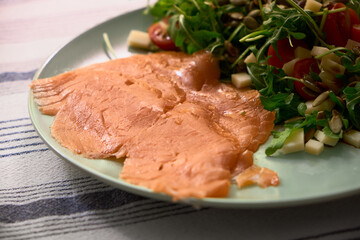 Close-up of salmon slices with arugula, cherry tomatoes, cheese, pumpkin seeds, and oil on an olive-colored plate. Fresh, healthy, and perfect for a cozy meal.