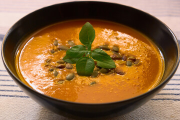Close-up of creamy pumpkin soup in a black bowl, garnished with fresh homemade basil and pumpkin seeds. Cozy autumn meal, perfect for seasonal cooking and healthy eating.