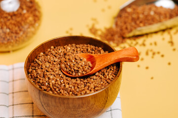 Buckwheat groats in a wooden bowl with a spoon on a yellow background