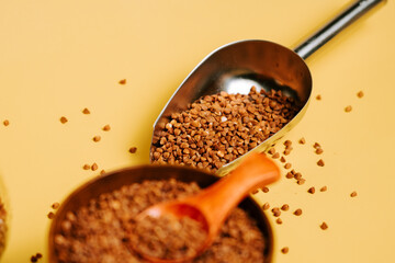 Buckwheat groats spilling from a scoop on a yellow background with a wooden measuring spoon