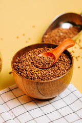Buckwheat groats in a wooden bowl with a spoon on a table with a yellow background