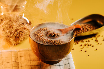 Buckwheat groats in a wooden bowl with steam rising on a bright yellow background